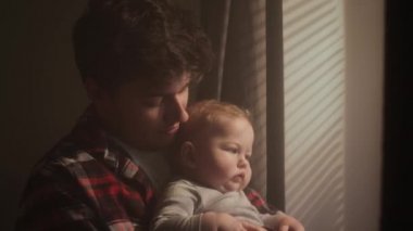 Bin yıllık bir baba, oğlunu evin penceresinden kollarına alır. Pencereden gelen güneş ışınları çocukların yüzünde parlıyor. Ebeveyn sarılması. Aile durur ve pencereden dışarı bakar.