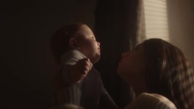 Gülümseyen bir kızın kollarında bir çocuk. Milenyum anneleri evlerinin penceresinde oğullarının kollarına kusar. Pencere perdeleri. Çocukların yüzü güneşe bakıyor. Sıcak sarı ton. Aile değerleri.