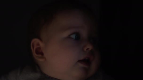 Bebek annesinin kollarında, mavi gözleriyle bakıyor. Millennial anne, oğlunu evin penceresinden kollarına aldı. Çocukların yüzü güneşe bakıyor. Yakın plan portre — Stok video