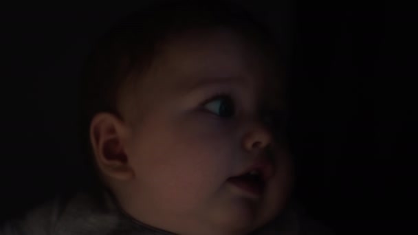 Das Baby liegt in den Armen seiner Mutter, blickt mit blauen Augen. Millennium-Mutter hält ihren Sohn am Fenster des Hauses in den Armen. Die Kinder stehen in der Sonne. Porträt aus nächster Nähe — Stockvideo