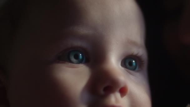 Primo piano cinematografico di un bambino occhi azzurri. Il bambino impara il mondo. Guarda la luce dalla finestra, i raggi solari. Comfort domestico, congedo di maternità. Ritratto di un bambino felice in una giornata di sole estiva — Video Stock