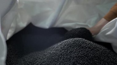 Bir adam çöp geri dönüşüm tesisinde ellerinden siyah polimer granüller döküyor.