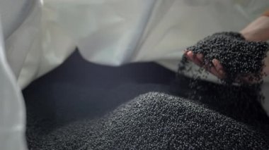 Eller çöp geri dönüşüm fabrikasındaki torbadan polimer granülleri kaldırır..