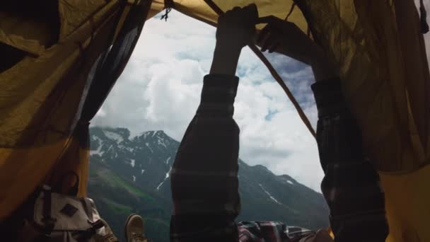 日落露营。一个穿着格子呢衬衫的女徒步旅行者坐在一个黄色的帐篷里，画像上，面带微笑。山区的远程自由应聘工作 — 图库视频影像