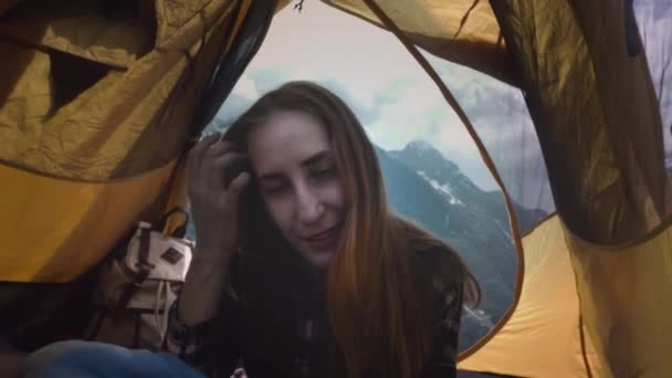 Zonsondergang kamperen. Een meisje wandelaar gekleed in een geruit shirt zit in een gele tent, portret, glimlachend. freelance werk op afstand in de bergen — Stockvideo