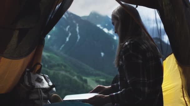 Eine junge Freiberuflerin nutzt einen Laptop, um im Freien zu arbeiten. Fernarbeit in einem gelben Zelt in der Nähe der großen Berge. — Stockvideo