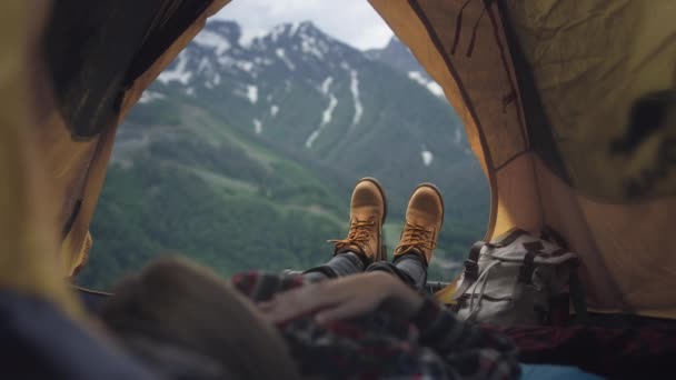 Frauenbeine in gelben Wanderschuhen liegen in einem gelben Zelt. Der Reisende ruht sich aus und bewundert nach dem Aufstieg die Berge — Stockvideo