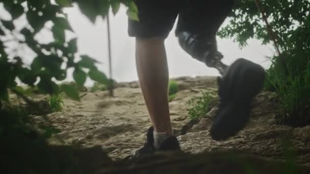 Чоловічий пішохід з протезною ногою. Людина з обмеженими можливостями пробиває скелі, насолоджуючись своїм часом під час подорожі в гори — стокове відео