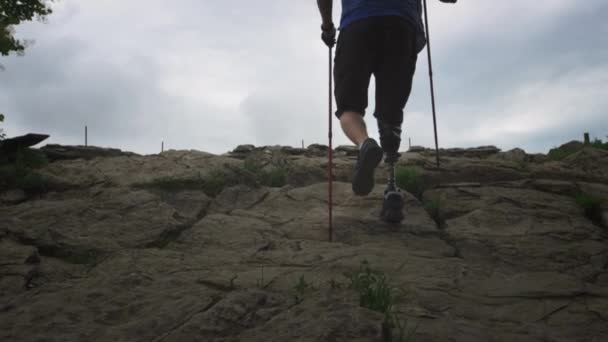 Чоловічий пішохід з протезною ногою. Людина з обмеженими можливостями пробиває скелі, насолоджуючись своїм часом під час подорожі в гори — стокове відео