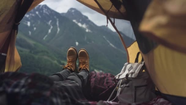 黄色のハイキングブーツの女性の足は黄色のテントの中にあります。登山後の山々を眺めながら、旅人は休んでいます。 — ストック動画