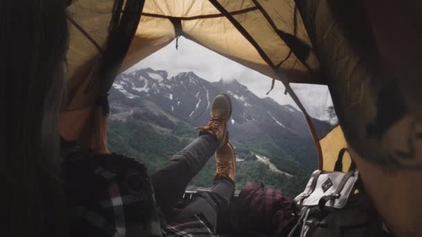 黄色のブーツのハイカーの女性の足は黄色のテントの中にあります。旅行者の足が休んでいる、少女は嘘をつき、登山後に山を賞賛します — ストック動画
