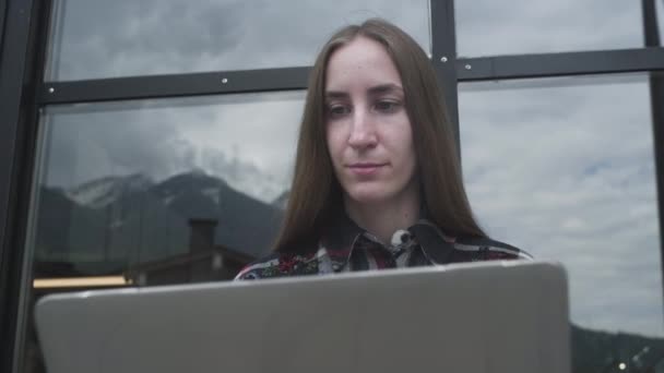 Молодая девушка-фрилансер работает за ноутбуком в кафе возле гор. Женщина печатает на ноутбуке, программы. — стоковое видео