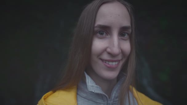 Portret van een blanke meisjesreiziger in een gele regenjas bij een waterval in het bos. Lifestyle concept, in slow motion — Stockvideo