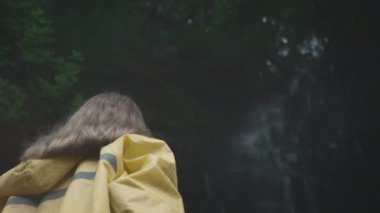 Sarı yağmurluklu beyaz kız gezgin ormandaki bir akıllı telefonda şelalenin fotoğrafını çekiyor..