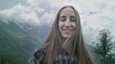 Dağların arka planında genç bir kızın portresi. Kadın gülümsüyor, kameraya bakıyor. Dağlarda seyahat et.
