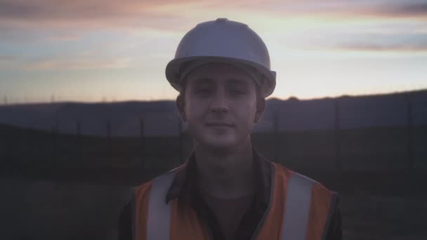 Portrait of a young engineer next to a plantation of solar panels during sunset. Checks the health and efficiency of renewable energy sources. — Stock Video