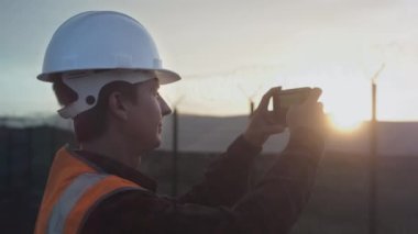 Erkek bir mühendis akıllı telefondan plantasyon ya da güneş paneli bitkisinin fotoğrafını çekiyor. Kurulumun kalitesini denetler ve kontrol eder