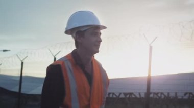 Profesyonel bir erkek mühendis güneş paneli çiftliğinin yanında yürüyor. Fotovoltaik tesisat tesisi. Yenilenebilir enerji teknolojileri