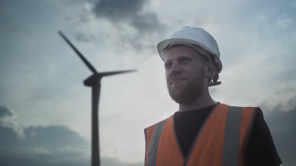 PORTRAIT : Jeune homme avec une barbe, dans un casque de protection blanc et un gilet, montre comme, pouce en l'air, approuve l'énergie verte. — Video