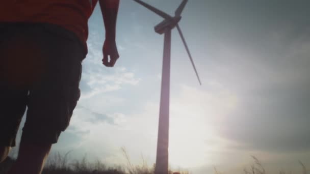 Een man met een witte helm en een vest rent naar een windturbine die een ongeluk repareert. Ingenieur of werknemer. Inspecteert en past de schroef aan — Stockvideo