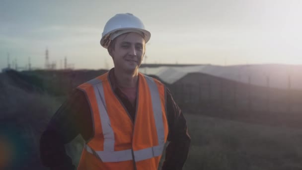 Retrato de um jovem engenheiro ao lado de painéis solares durante o pôr do sol. Verifica a saúde e a eficiência das fontes de energia renováveis e das células solares. Plantação de painéis solares. Conceito de energia verde — Vídeo de Stock