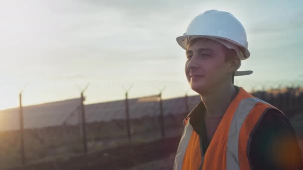 Retrato de um jovem engenheiro ao lado de uma plantação de painéis solares e fotovoltaicos durante o pôr do sol. — Vídeo de Stock