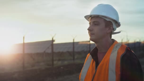 Porträt eines jungen Ingenieurs neben einer Plantage von Sonnenkollektoren bei Sonnenuntergang. Überprüfung der Gesundheit und Effizienz erneuerbarer Energiequellen. — Stockvideo