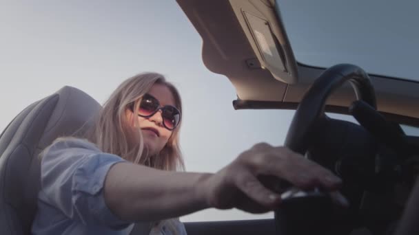 Une jeune fille au volant d'une décapotable commute la boîte automatique. Commence à bouger. Le début d'un voyage, d'un road trip. — Video