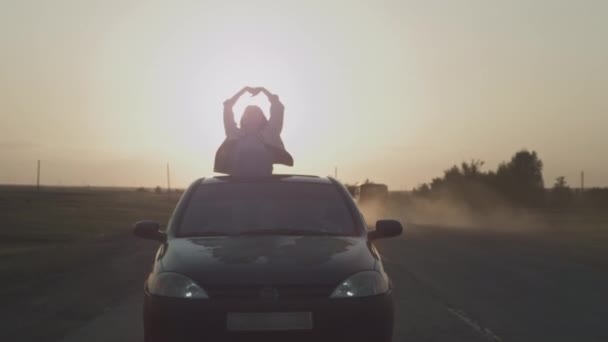 Jovem menina bonita cavalga no carro com as mãos levantadas para cima, uma mulher no teto solar do carro. Viagem de carro aventura, wonderlast. — Vídeo de Stock