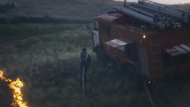 UFA RUSSIA - 07.08.2021: A real Firefighter extinguishes a burning flame from a hose with water. Nature is on fire. Water from a hose is sprayed onto the fire. There is a fire engine nearby. — Stock Video