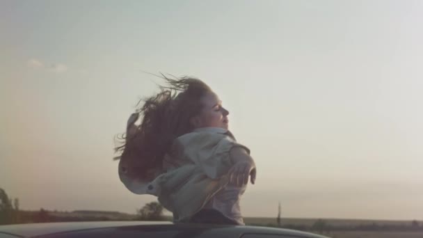 Jovem menina bonita cavalga no carro com as mãos levantadas para cima, uma mulher no teto solar do carro. Viagem de carro aventura, wonderlast. — Vídeo de Stock