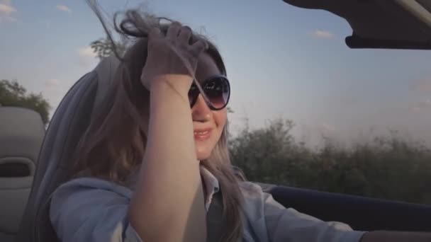Młoda piękna dziewczyna jeździ latem kabrioletem sportowym. Lubi życie o zachodzie słońca w samochodzie bez dachu, kabriolecie. Włosy na wietrze w zwolnionym tempie. — Wideo stockowe