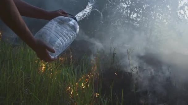 A volunteer man or boy extinguishes a wild fire. Pours water from a plastic bottle. Rain forest wildfire disaster, dry bushes burning, fire reasons. — Stock Video