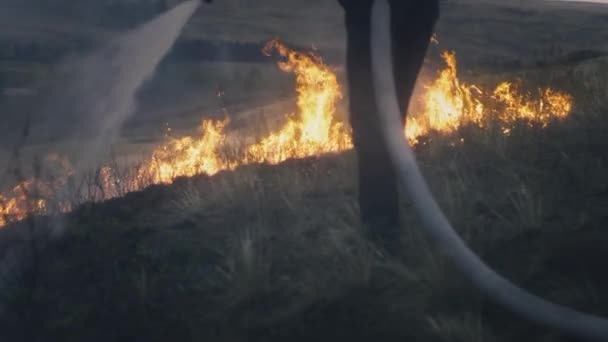 Hasič drží hadici s vodou v rukou a uhasí hořící plamen. Příroda hoří: tráva, stepi, lesy a pole