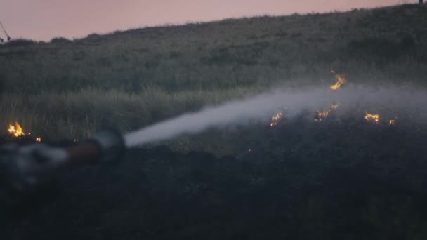 Egy tűzoltó vizet tart a kezében, kioltja az égő lángot. Természetes tárgyak égnek: fű, sztyepp, erdők — Stock videók