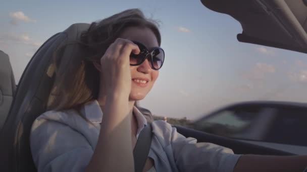 Young beautiful girl drives a convertible sport car in summer. Enjoys life at sunset in a roofless car, cabriolet. Hair in the wind in slow motion. — Stock Video