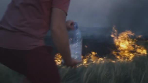 Ein freiwilliger Mann oder Junge löscht einen Flächenbrand. Gießt Wasser aus einer Plastikflasche. Waldbrandkatastrophe im Regenwald, trockene Büsche brennen, Brandursache. — Stockvideo