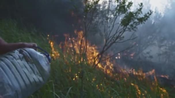 Um homem ou rapaz voluntário extingue um incêndio selvagem. Despeja água de uma garrafa de plástico. Desastre de floresta tropical, arbustos secos queimando, razões de fogo. — Vídeo de Stock