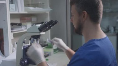 Mavi ceketli doktor bir bilim adamı gözleriyle mikroskobun gözlerinden bakıyor. Makro fotoğrafçılık için lens ayarlar