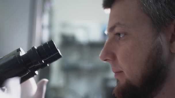 Ученый-врач в белом халате смотрит глазами в окуляры микроскопа. Установка объективов для макросъемки клеток — стоковое видео