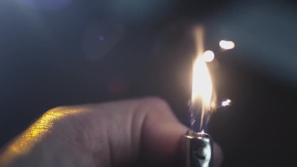 Un briquet à gaz dans une main humaine s'allume au ralenti. Une flamme de feu illumine une pièce sombre, brûle d'étincelles sur un fond abstrait noir — Video