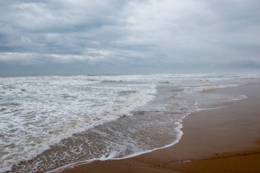 Kumsalda fırtınalı bir gün, dalgalı sular bulutlu gökyüzü.