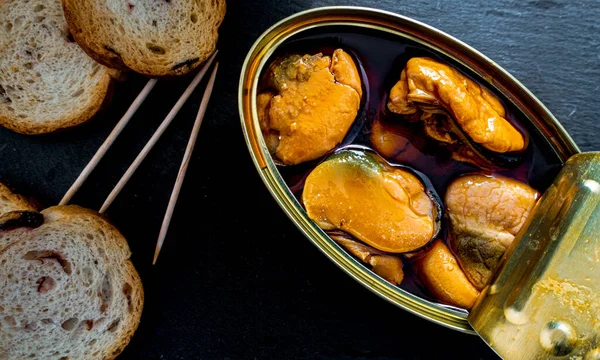 Siyah bir tabakta konserve midye ve ekmek ekmeği.