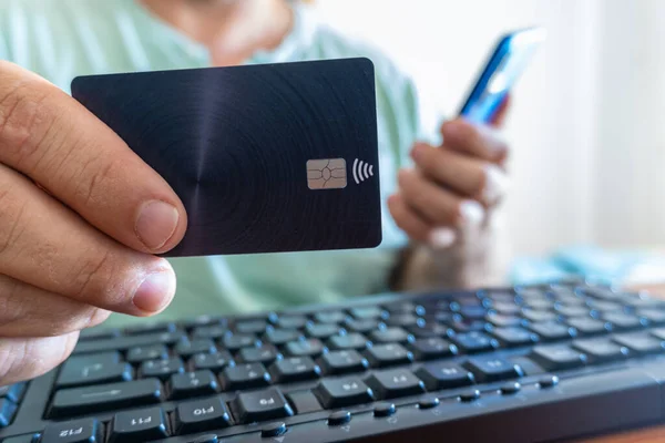 Modern bir kredi kartı olan, bilgisayar klavyesi olan ve akıllı telefonlu odaklanmamış bir geçmişi olan bir erkek. İş ve ekonomi kavramı.