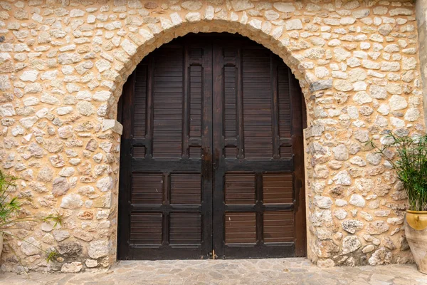 Large, solid wooden door at the entrance of a house, with stone walls.