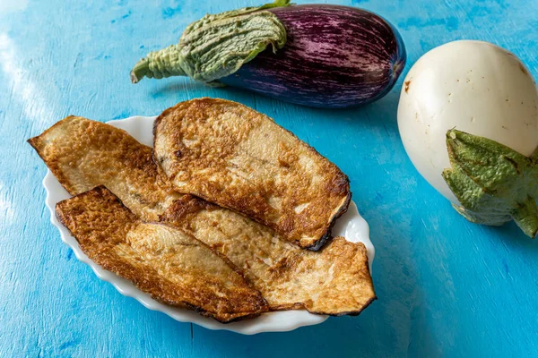 Patlıcan ezildi ve yağda kızardı, mavi ahşap bir arka planda ve iki patlıcan ile kompozisyonu süslüyor..