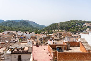 Arka planda dağlar ve sabahları açık bir gökyüzü olan bir kasabanın çatılarını görmek..