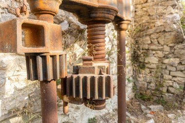 Arka planda taş bir duvar olan terk edilmiş ve paslı yağ preslerinin detayları..