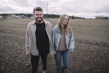 Birbirine aşık bir çift, bulutlu bir havada açık soya fasulyesi tarlasında yürür ve bol bol sarılır.