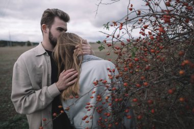 Birbirine aşık bir çift, bulutlu bir havada açık soya fasulyesi tarlasında yürür ve bol bol sarılır.